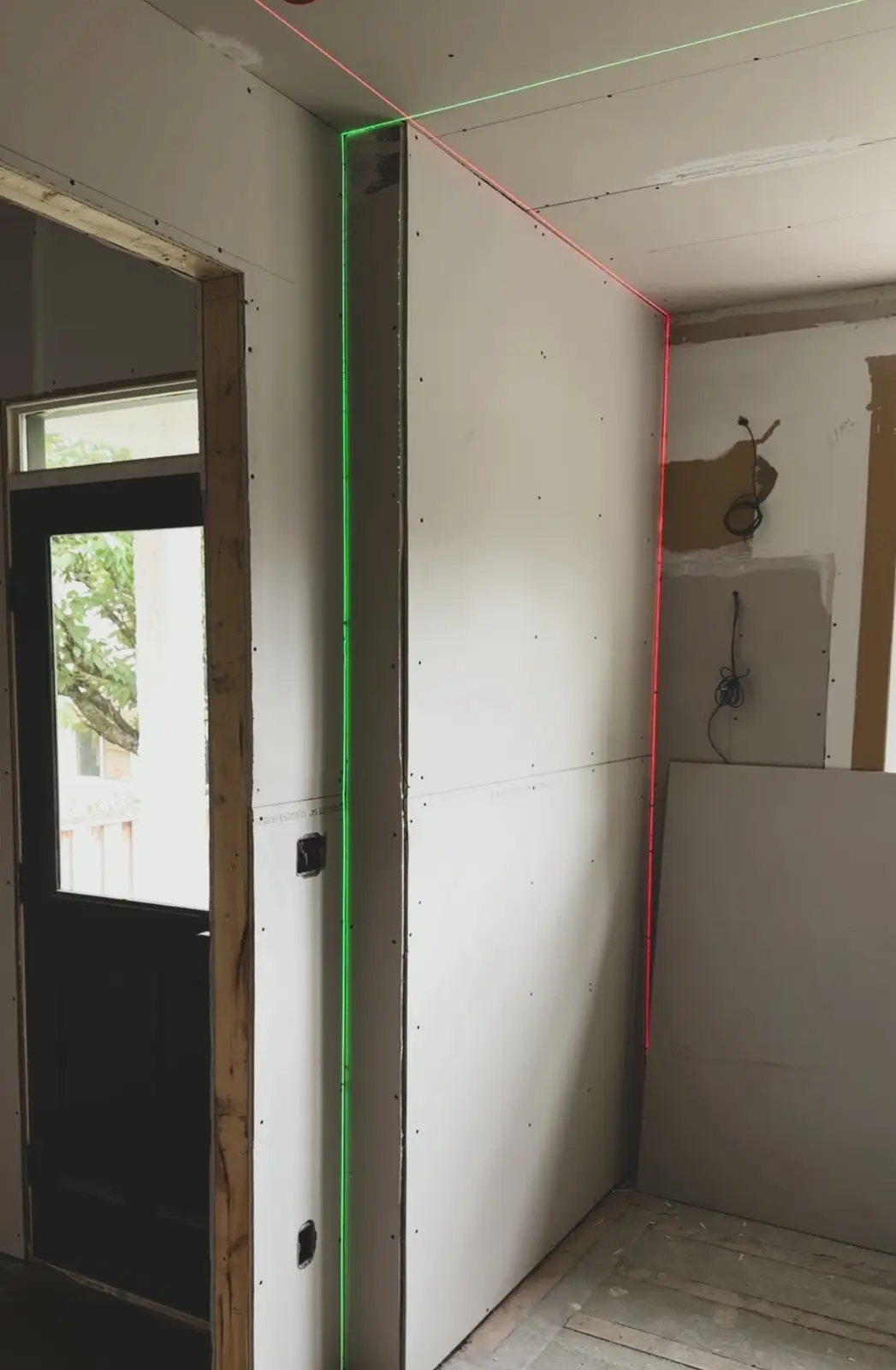 Green and red laser lines running down a boarded corner and along the ceiling line before taping.