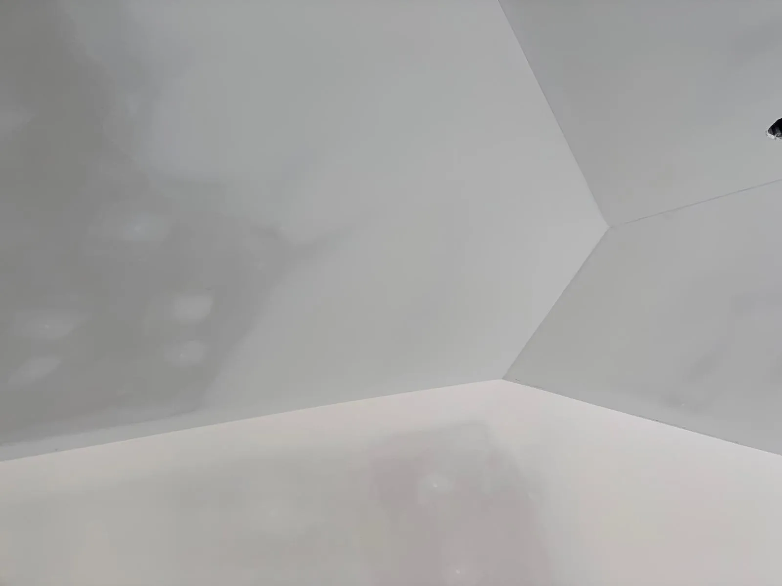 A sanded ceiling before paint, four planes meeting at a point, the seams reading as clean lines under the light.